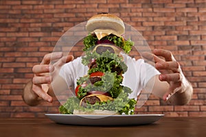 Hungry man with huge burger at wooden table