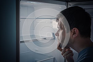 Hungry man is looking for food to eat in empty fridge at night