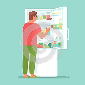 Hungry man opens a refrigerator full of food and drinks in order to have a snack or take food for cooking
