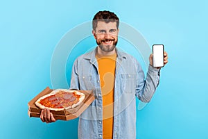 Hungry man with pizza box shows smartphone blank screen, studio