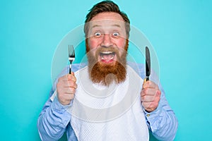 Hungry man with tattoos is ready to eat with cutlery in hand