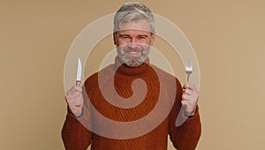 Hungry middle-aged man with fork, knife waiting for serving dinner dishes with cutlery, meal lunch