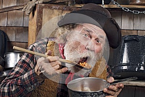 Hungry old cowboy eating beans from a saucepan