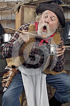 Hungry old cowboy eating beans from a saucepan