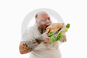 Hungry overweigh bearded man enjoying eating huge burger . Unhealthy food concept