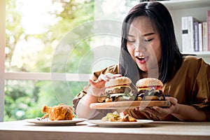 Hungry overweight woman holding hamburger on wooden plate after delivery man delivers foods at home. Concept of binge eating photo