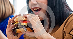 Hungry overweight woman smiling and holding hamburger and sitting in the living room, her very happy and enjoy to eat fast food. C