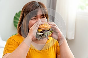 Hungry overweight young asian woman holding hamburger, Her hungry all time and overeat, gluttony and binge eating. Her lifestyle photo