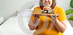 Hungry overweight young asian woman holding hamburger, Her hungry all time and overeat, gluttony and binge eating. Her lifestyle