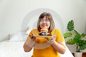 Hungry overweight young asian woman holding hamburger, Her hungry all time and overeat, gluttony and binge eating. Her lifestyle