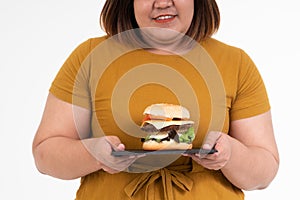 Hungry overweight young Asian woman holding hamburger on isolated background, Her hungry all time and overeat, gluttony and binge