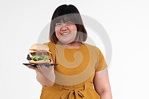 Hungry overweight young Asian woman holding hamburger on isolated background, Her hungry all time and overeat, gluttony and binge