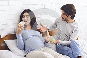 Hungry pregnant woman eating croissant instead of green apple