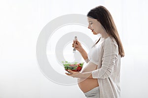 Hungry pregnant woman eating healthy vegetable salad, side view
