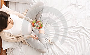 Hungry pregnant woman enjoying fresh vegetable salad in bed