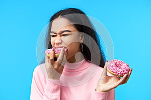 Hungry pretty girl eating donuts isolated over blue background