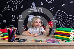 Hungry schoolgirl sitting at the desk with books, school supplies, holding in her arm red apple ready to bite