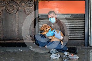 Hungry sick homeless beggar man on the street with his dog begging for money and food to eat wearing the medicine mask and gloves