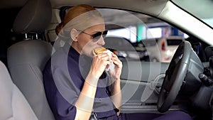 Hungry woman cop eating burger sitting in police car in parking lot, junk food