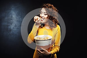 Hungry woman eats handful of popcorn while waiting for movie