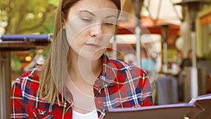 Hungry woman sitting in cafe looking at menu. Smiling beautiful female choosing food at restaurant