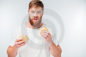 Hungry young bearded man holding two hamburgers