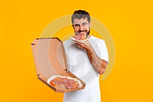 Hungry young European man bites into slice of pizza, studio