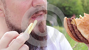 Hungry young man with a beard eats a delicious burger and french fries