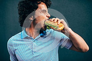 Hungry young man eating a cheeseburger has pleasant expression. Caucasian man in a fast food restaurant eating a hamburger