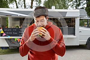 Hungry young man eating hamburger at food truck