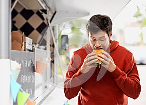 Hungry young man eating hamburger at food truck