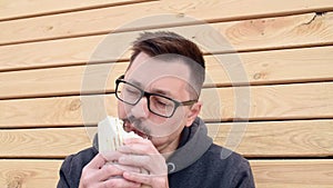 Hungry, young man eating kebab outdoor. Portrait of a middle aged guy dressed in a T-shirt and grey hoodie enjoying