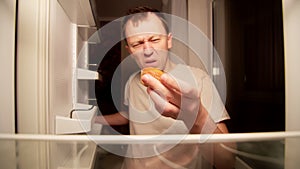 Hungry young man finds spoiled cupcake in the refrigerator at night