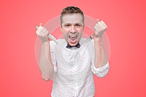 Hungry young man holding fork and knife on hand ready to eat, licking lips.