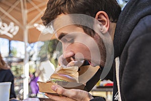 Hungry young man is sitting at the cafee terrace. He is looking at his burger, his mouth is wide open photo