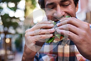 Hungry young man sitting outside biting into a delicious bagel