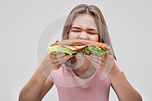 Hungry young woman bite burger. She devour it. Isolated on grey background.