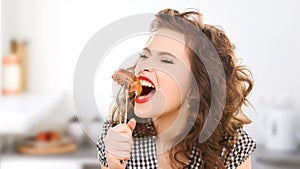 Hungry young woman eating meat on fork in kitchen