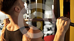 Hunky man doing pull-down exercise in gym with sunlight falling onto his back