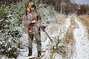 Hunter with a backpack and a hunting gun in the winter forest.