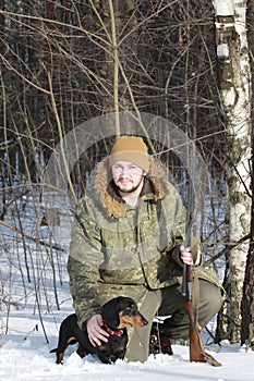 Hunter with black dachshund and shotgun in winter forest