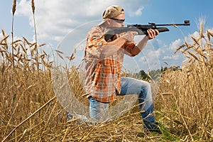 Hunter on cap and sunglasses aiming a gun at field