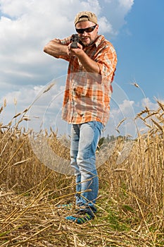 Hunter in cap and sunglasses aiming a gun at field