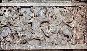 Hunter kills lions on the hunt, carved sculpture on historical wall of indian stone temple Hoysaleswara, India.