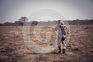 Hunter man camouflage with shotgun and backpack going through rural field during hunting