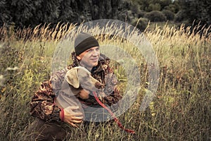 Hunter man with hunting dog Weimaraner in tall grass in rural field during hunting