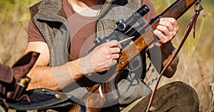 Hunter man. Hunting period. Male with a gun, rifle. Man is charging a hunting rifle. Close up. Process of hunting during photo