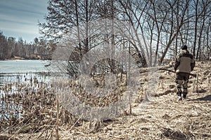 Hunter man walking along river bank during spring hunting season