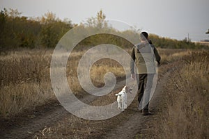 Hunter with Russian spaniel dog walking on the dirt road.