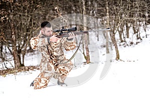 Hunter with sniper rifle aiming and shooting during winter